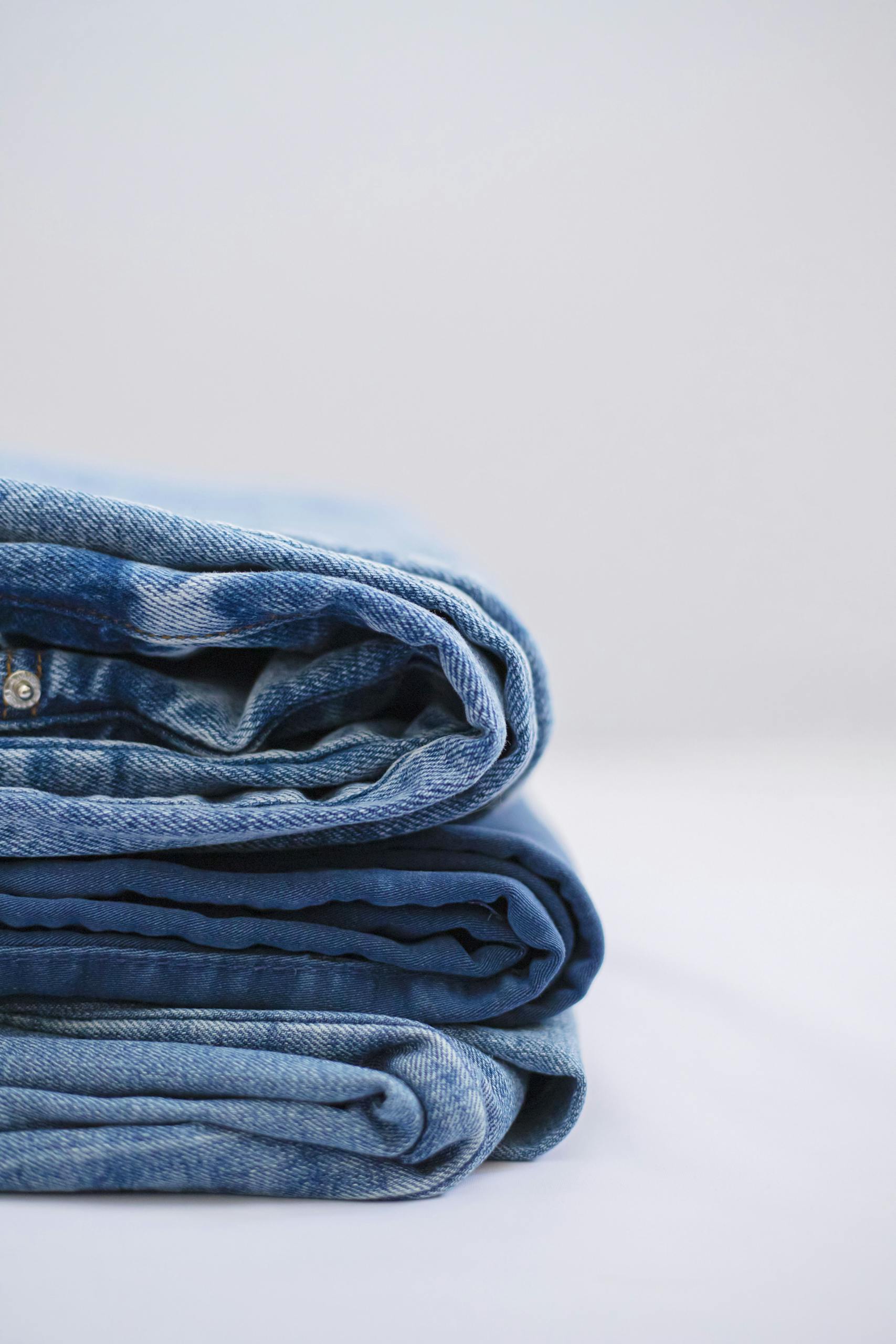 Close-up of a neatly folded stack of blue denim jeans against a plain background.