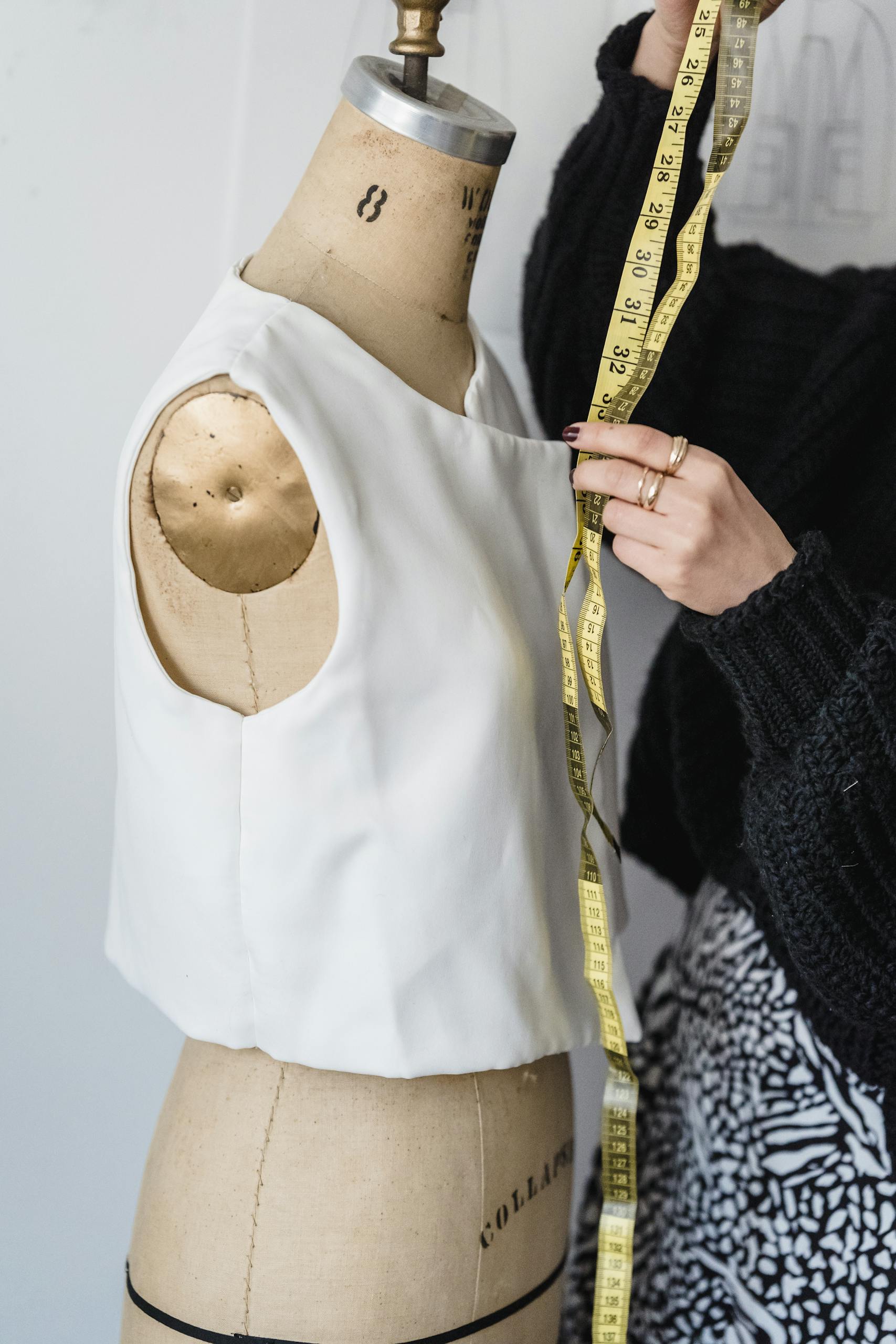 Crop unrecognizable female dressmaker working with measuring tape and mannequin in white tank top